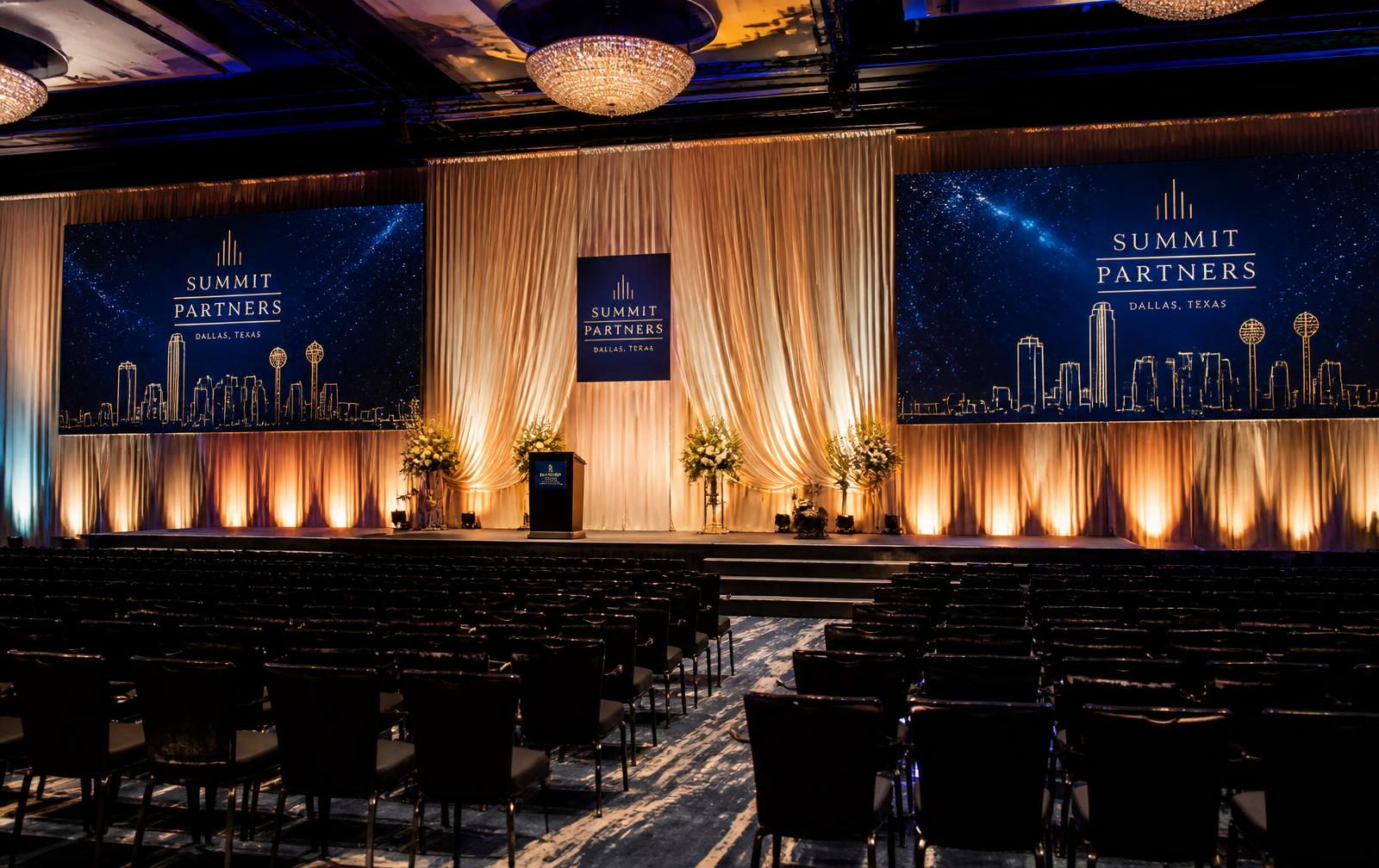 Corporate conference setup with theater-style seating and LED video walls flanking an elegant draped stage