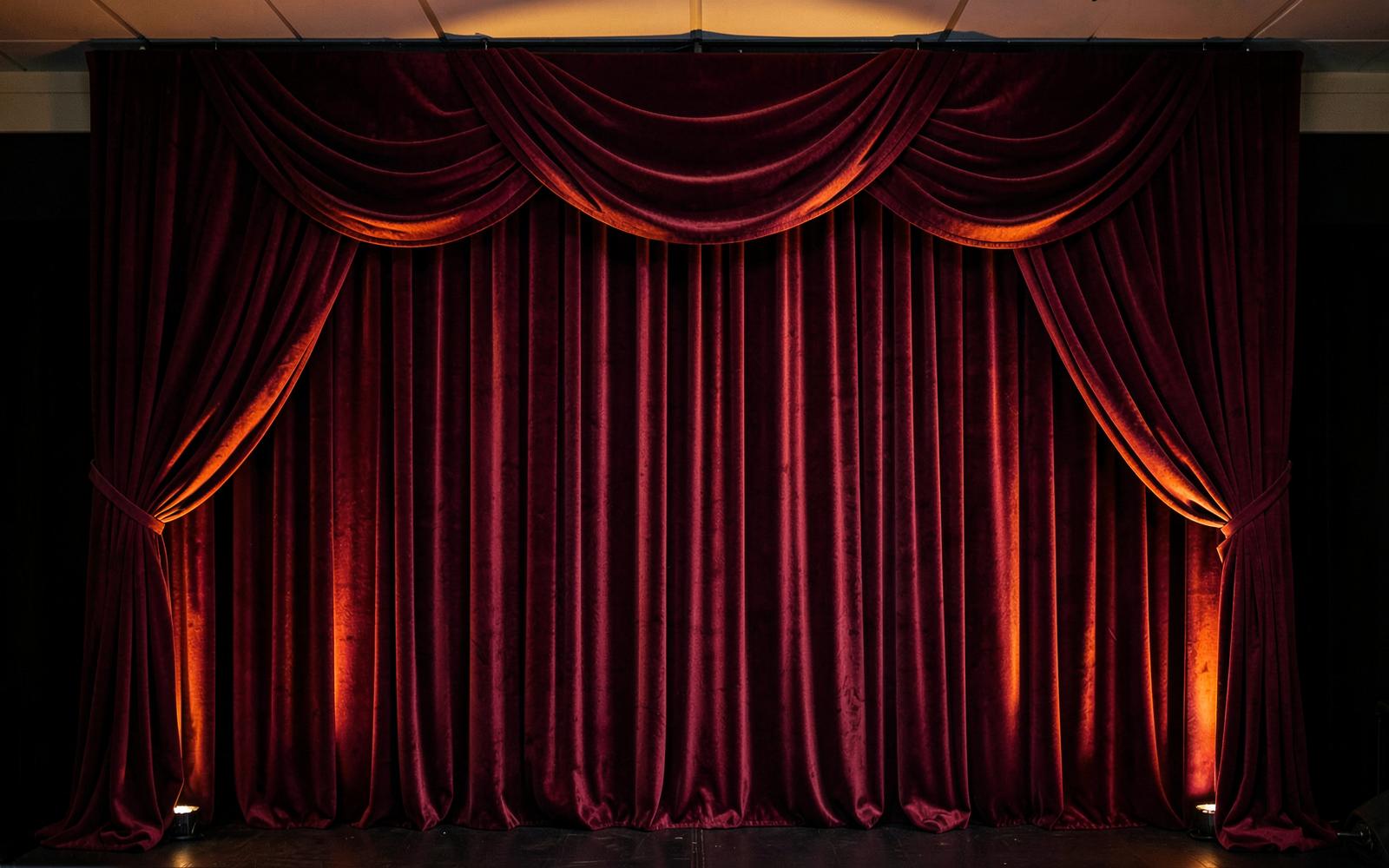 Pleated burgundy velour stage backdrop with swag valance and warm uplighting